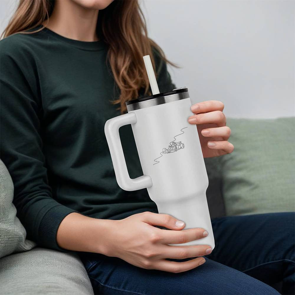 Person holding a white F1 merch tumbler water bottle featuring a black illustrated track and race car