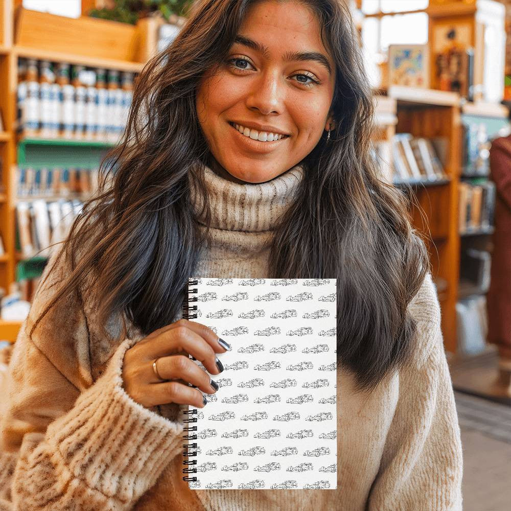 Woman holding an F1 fan inspired merch journal that's white with small black F1 cars