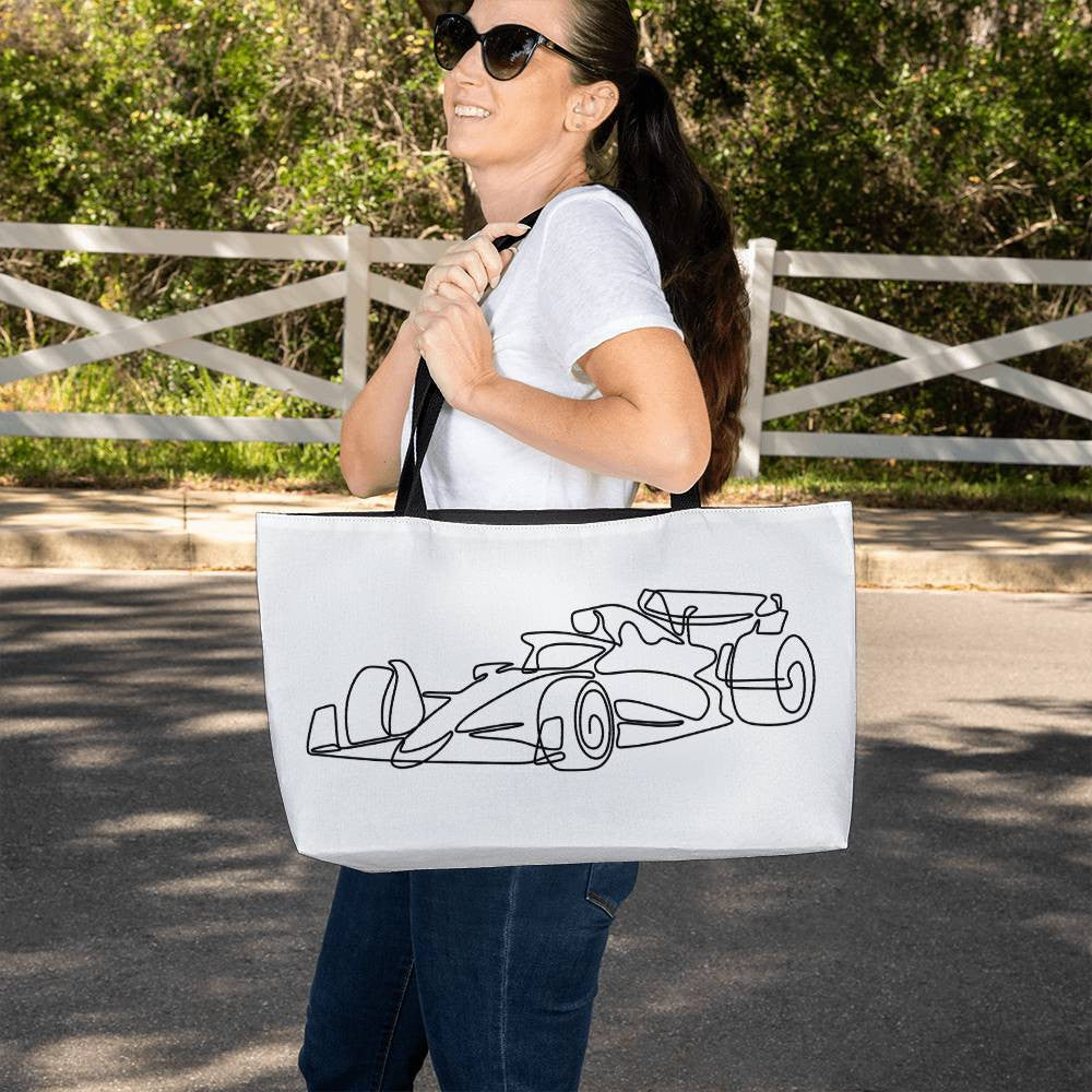 person holding white F1 tote bag featuring illustrated F1 race car for scale